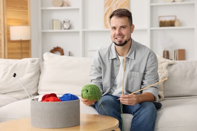 Photo of Man with green yarn and knitting needles on sofa at home