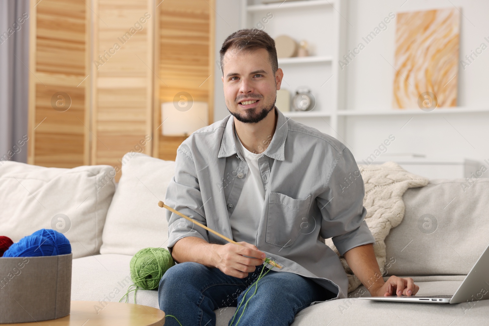 Photo of Man learning to knit with online course on sofa at home