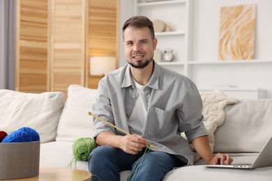 Man learning to knit with online course on sofa at home