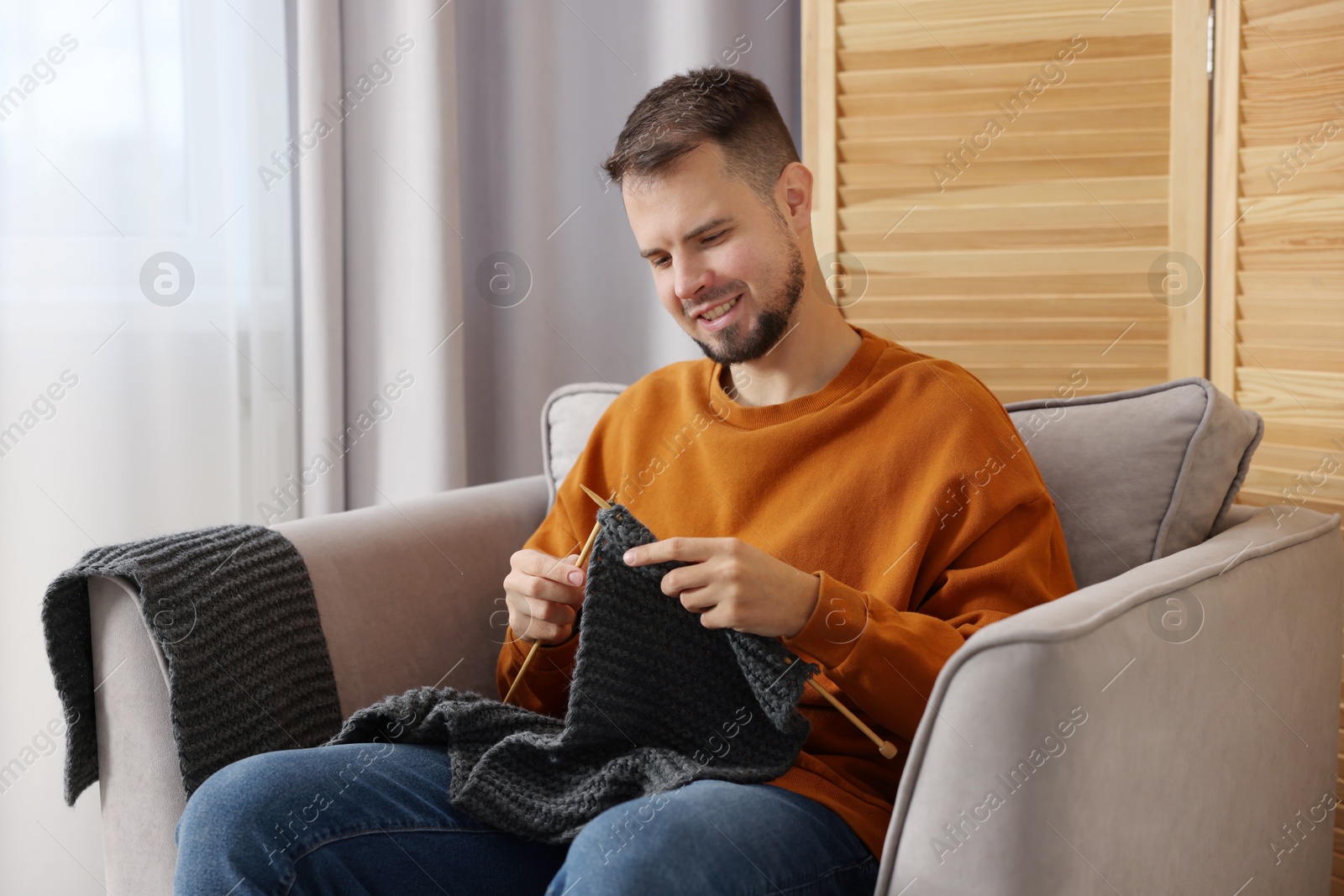 Photo of Man knitting with needles in armchair at home