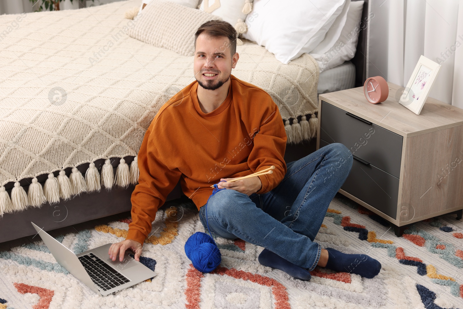 Photo of Man learning to knit with online course on floor at home