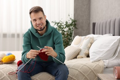 Photo of Man knitting with needles on bed at home