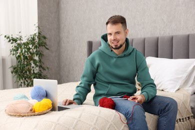 Man learning to knit with online course on bed at home