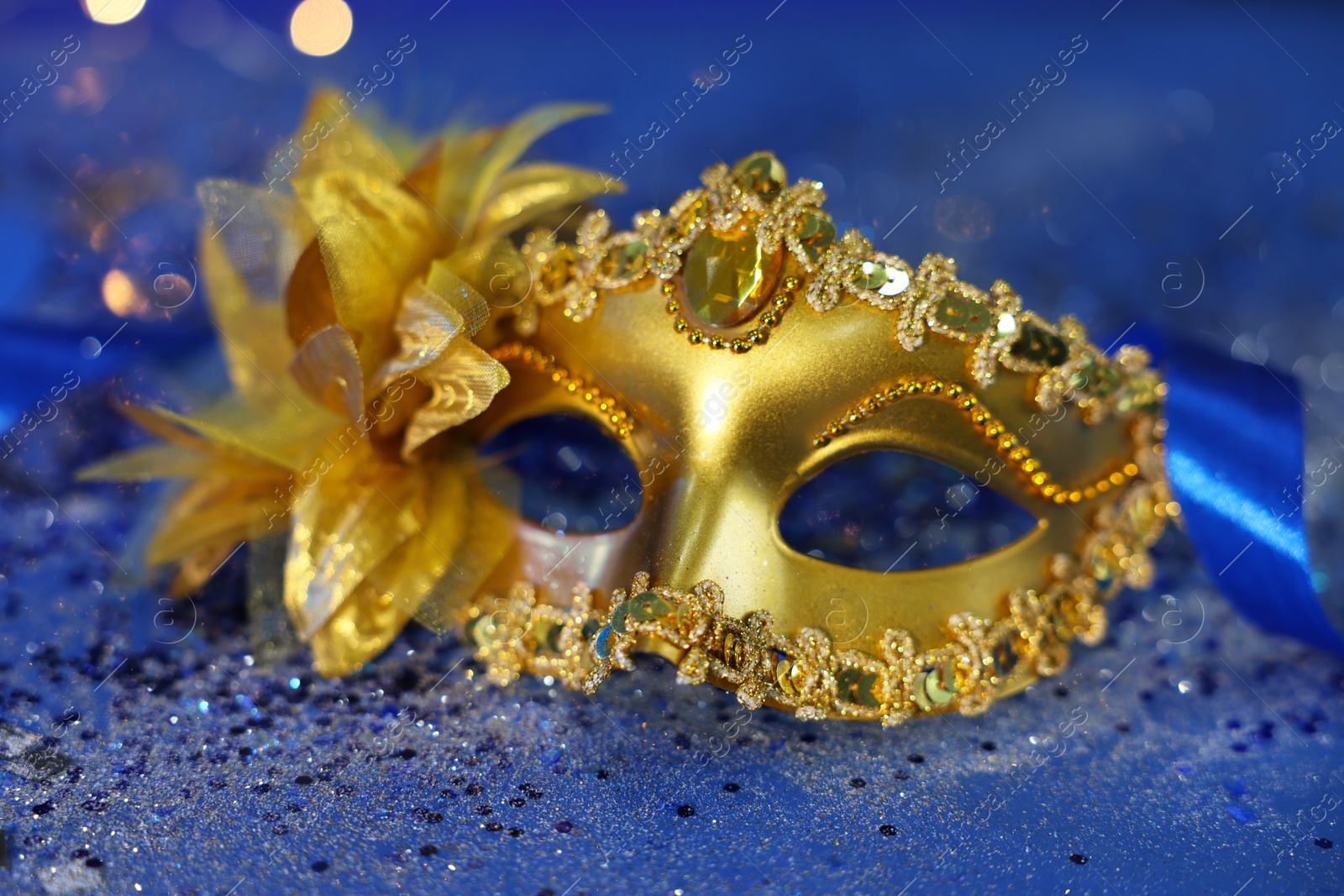 Photo of Beautiful carnival mask on blue glitter background, closeup