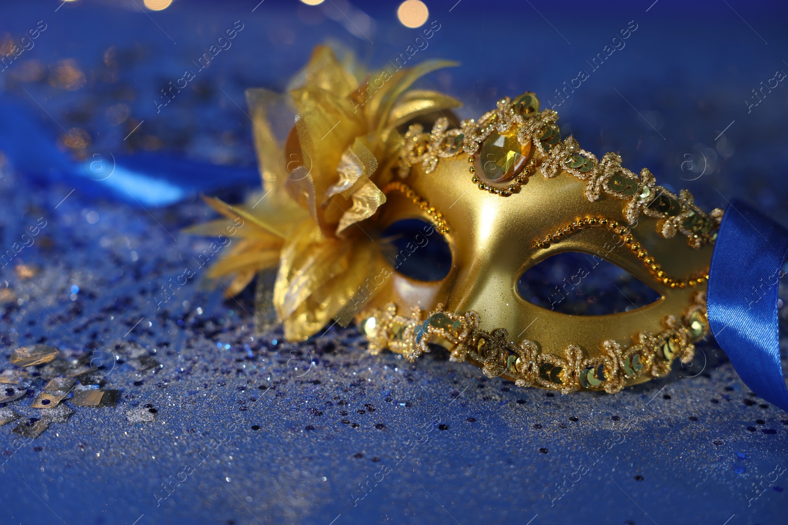 Photo of Beautiful carnival mask on blue glitter background, closeup