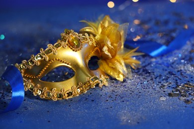 Photo of Beautiful carnival mask on blue glitter background, closeup