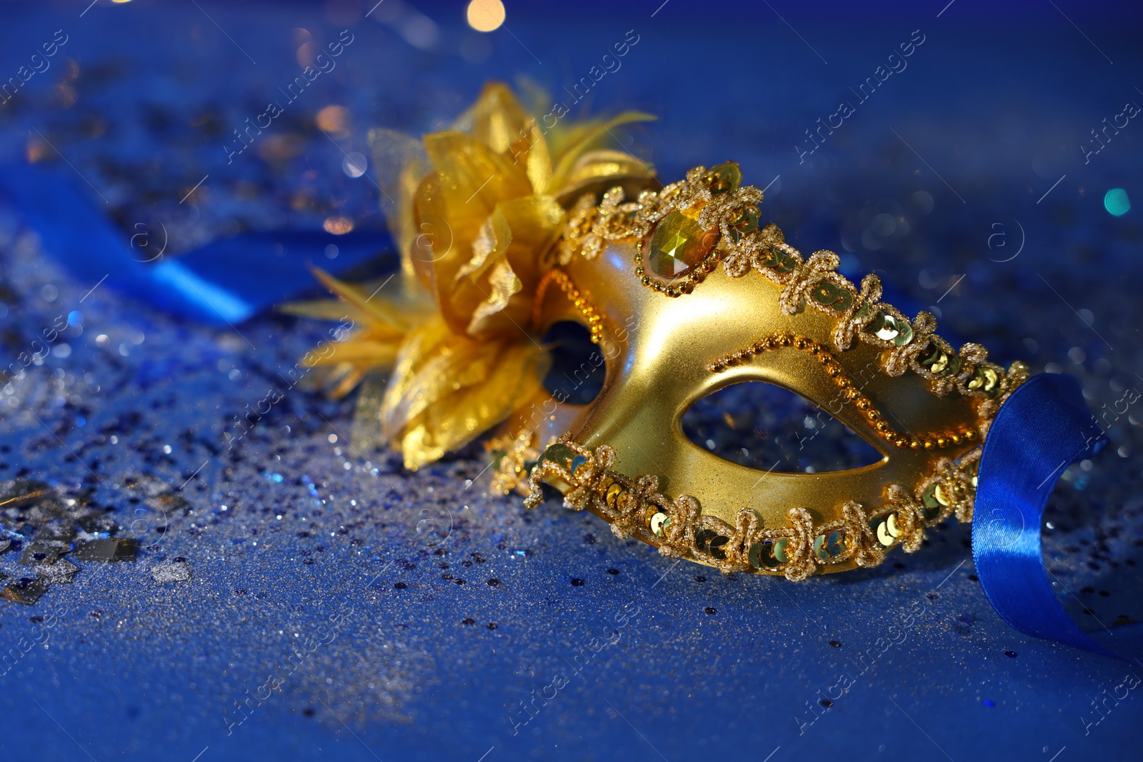 Photo of Beautiful carnival mask on blue glitter background, closeup