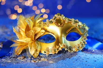 Photo of Beautiful carnival mask on blue glitter background against blurred lights, closeup. Bokeh effect