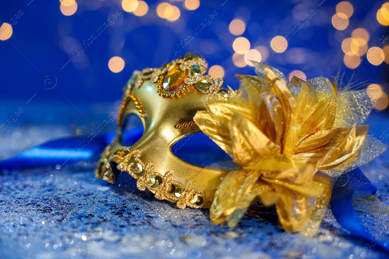 Photo of Beautiful carnival mask on blue glitter background against blurred lights, closeup. Bokeh effect