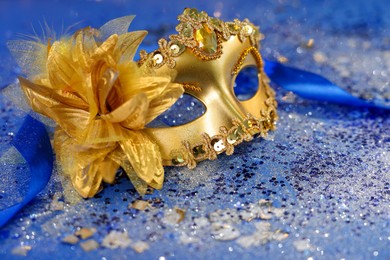 Photo of Beautiful carnival mask on blue glitter background, closeup