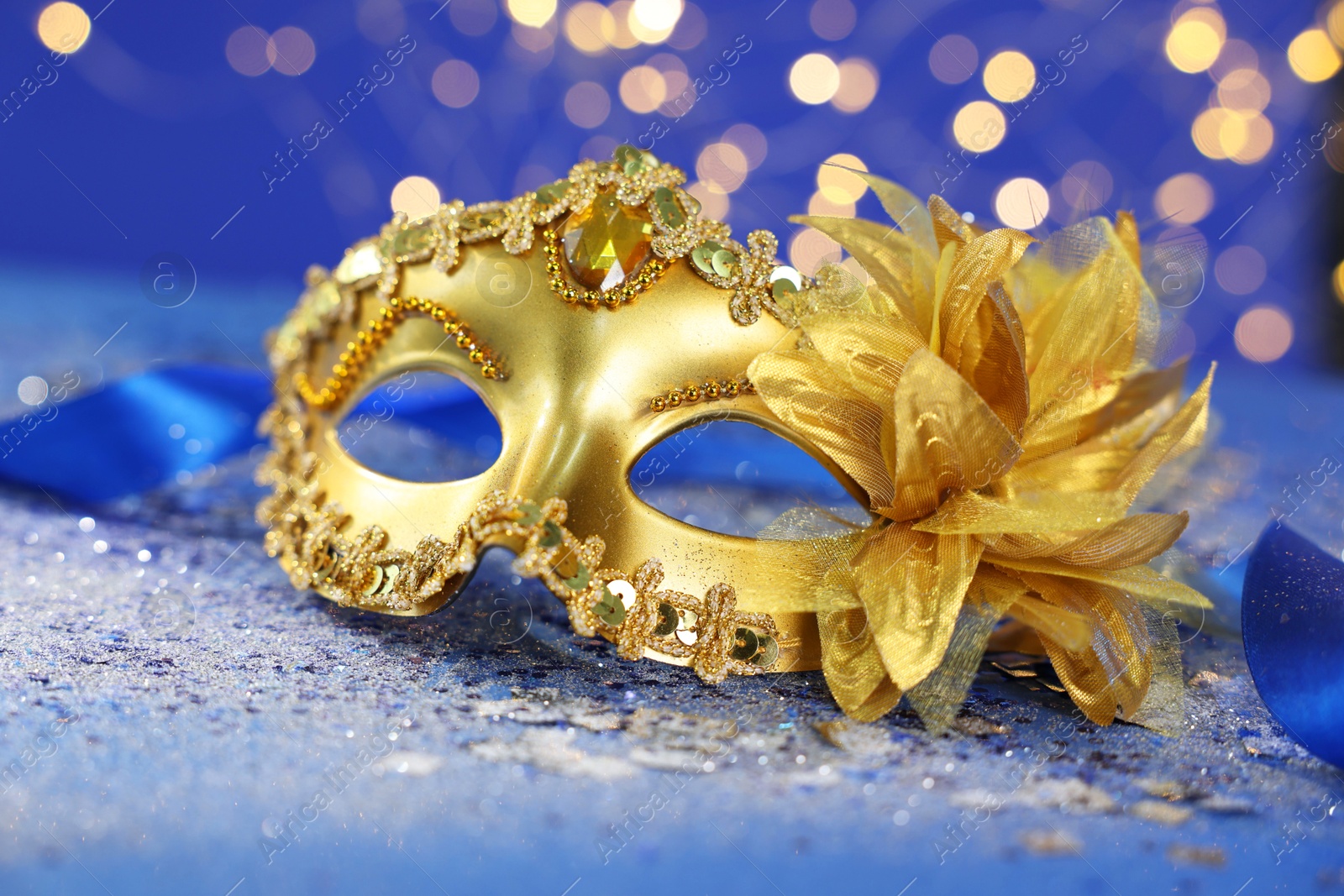 Photo of Beautiful carnival mask on blue glitter background against blurred lights, closeup. Bokeh effect