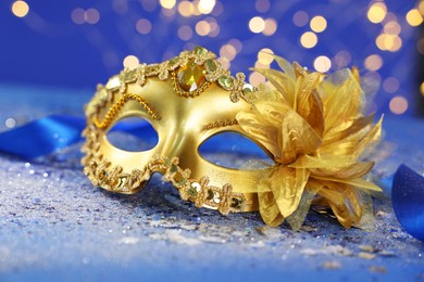 Photo of Beautiful carnival mask on blue glitter background against blurred lights, closeup. Bokeh effect