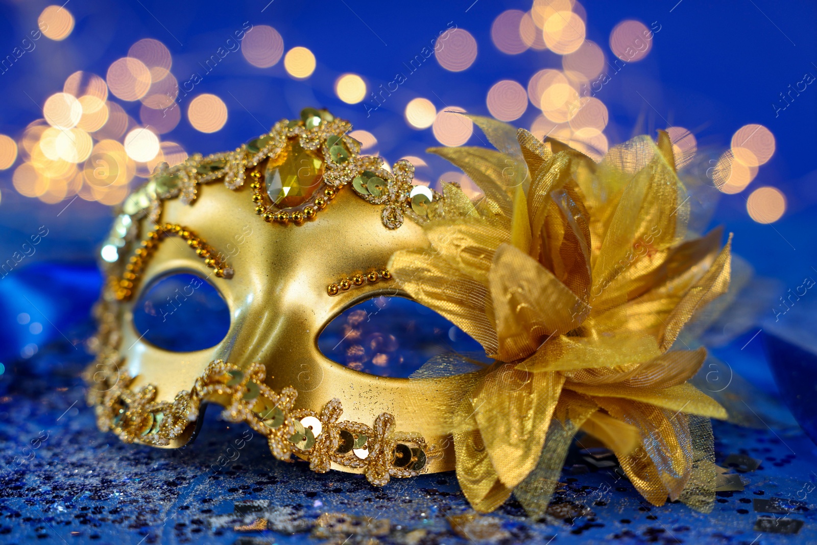 Photo of Beautiful carnival mask on blue glitter background against blurred lights, closeup. Bokeh effect