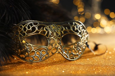 Photo of Beautiful carnival mask and black feathers on golden background against blurred lights, closeup. Bokeh effect