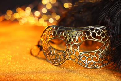 Photo of Beautiful carnival mask and black feathers on golden background against blurred lights, closeup. Bokeh effect