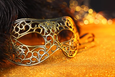 Photo of Beautiful carnival mask and black feathers on golden background against blurred lights, closeup. Bokeh effect