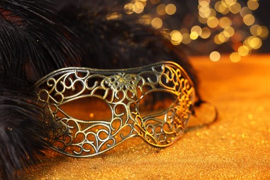 Photo of Beautiful carnival mask and black feathers on golden background against blurred lights, closeup. Bokeh effect