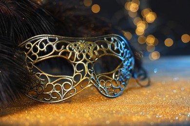 Photo of Beautiful carnival mask and black feathers on golden background against blurred lights, closeup. Bokeh effect