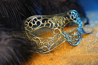 Photo of Beautiful carnival mask and black feathers on golden background, closeup