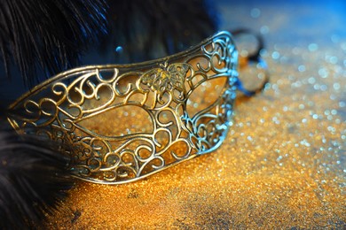 Photo of Beautiful carnival mask and black feathers on glitter background, closeup