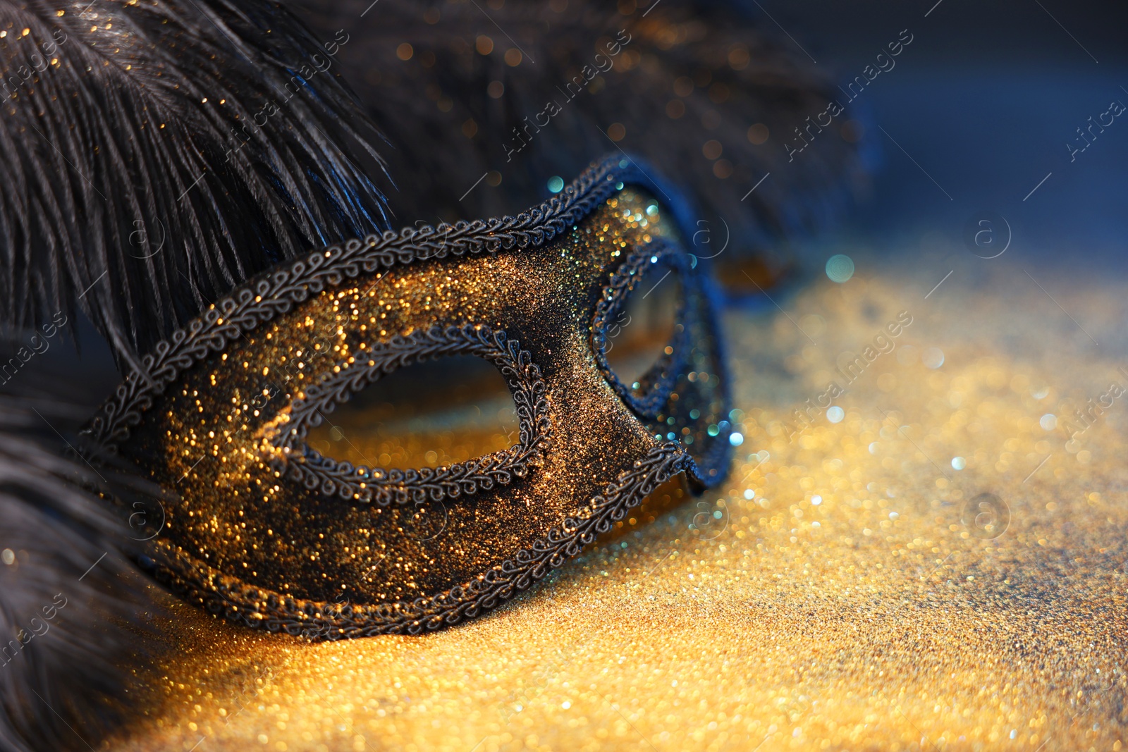 Photo of Beautiful carnival mask and black feathers on glitter background, closeup