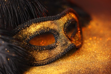 Photo of Beautiful carnival mask and black feathers on glitter background, closeup