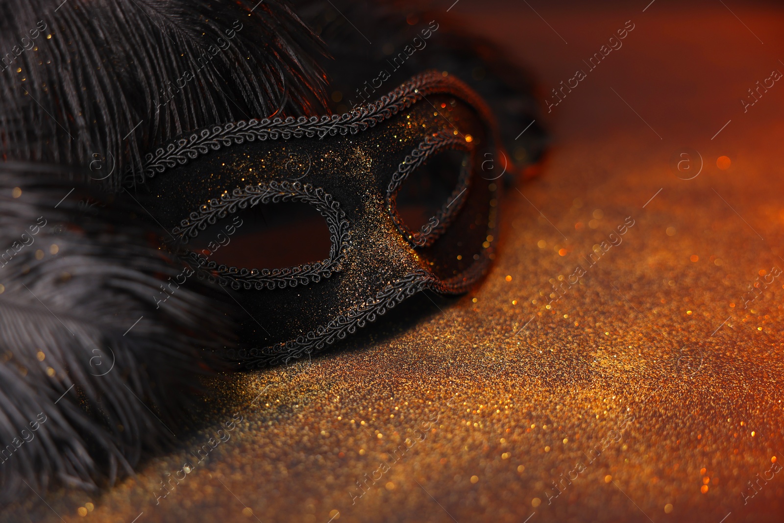 Photo of Beautiful carnival mask and black feathers on glitter background, closeup. Space for text