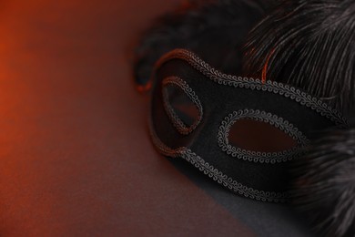 Photo of Beautiful carnival mask and feathers on black background in color lights, closeup. Space for text