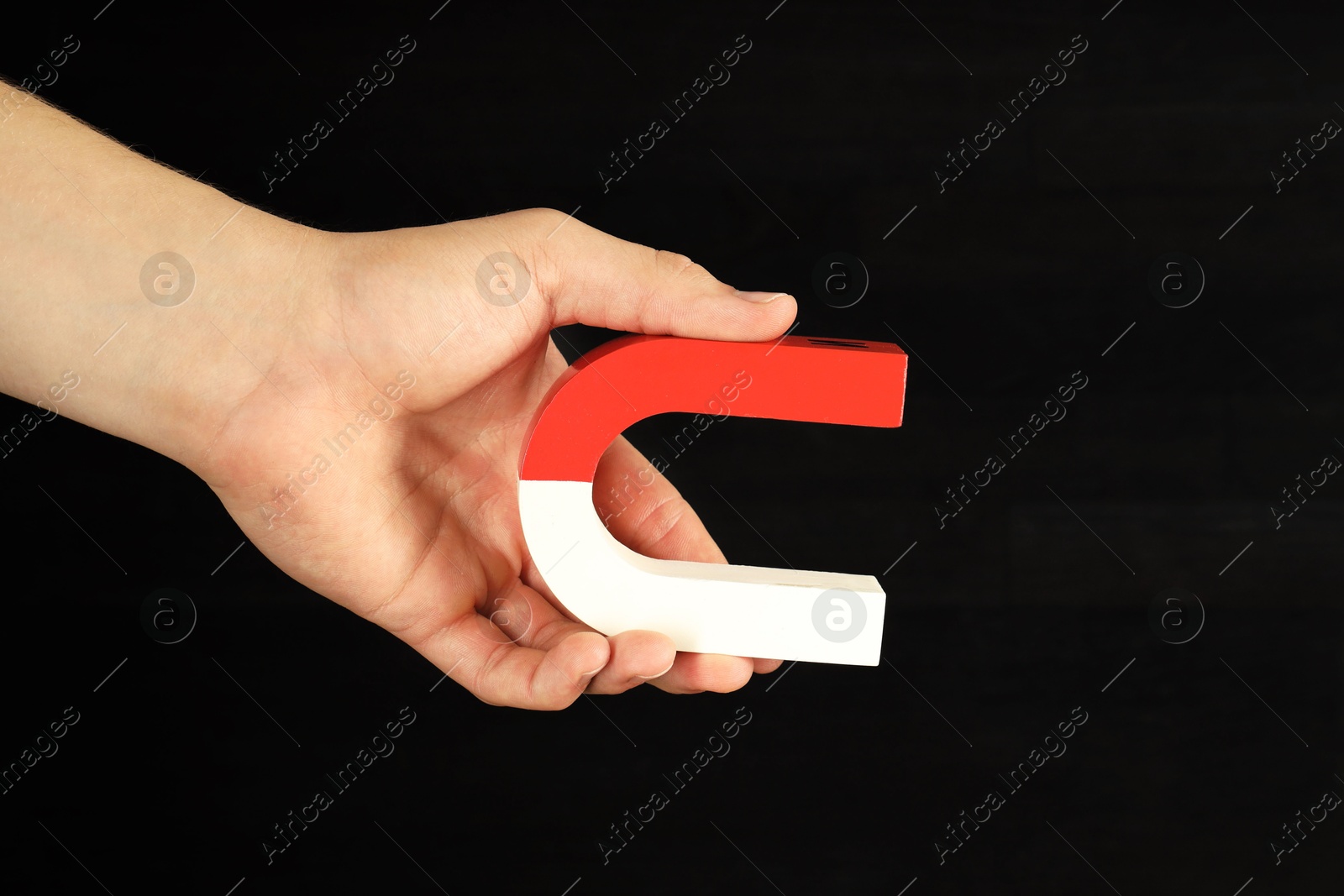 Photo of Man holding horseshoe magnet on dark background, closeup