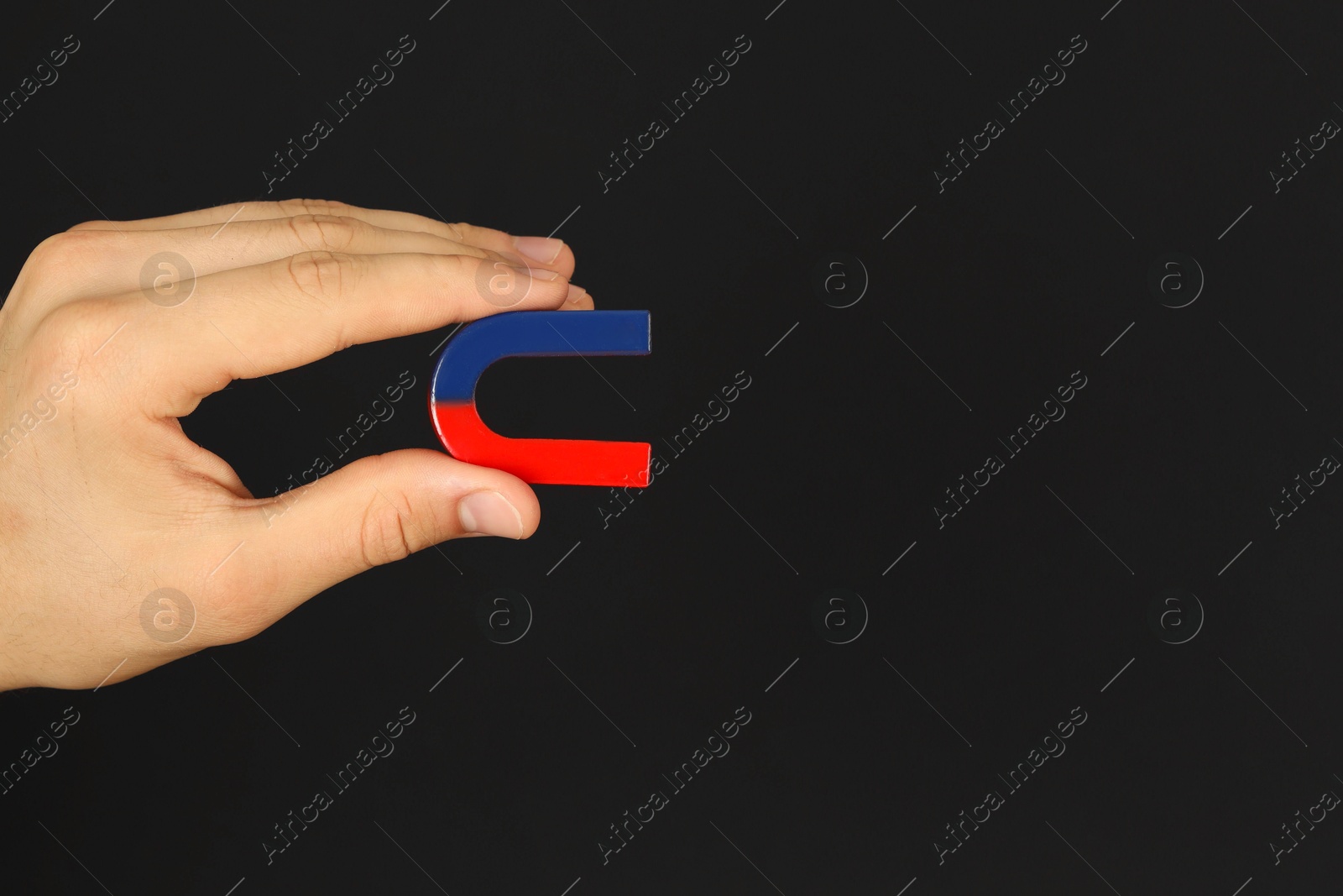 Photo of Man holding horseshoe magnet on dark background, closeup. Space for text