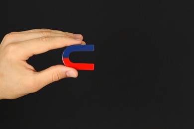 Photo of Man holding horseshoe magnet on dark background, closeup. Space for text