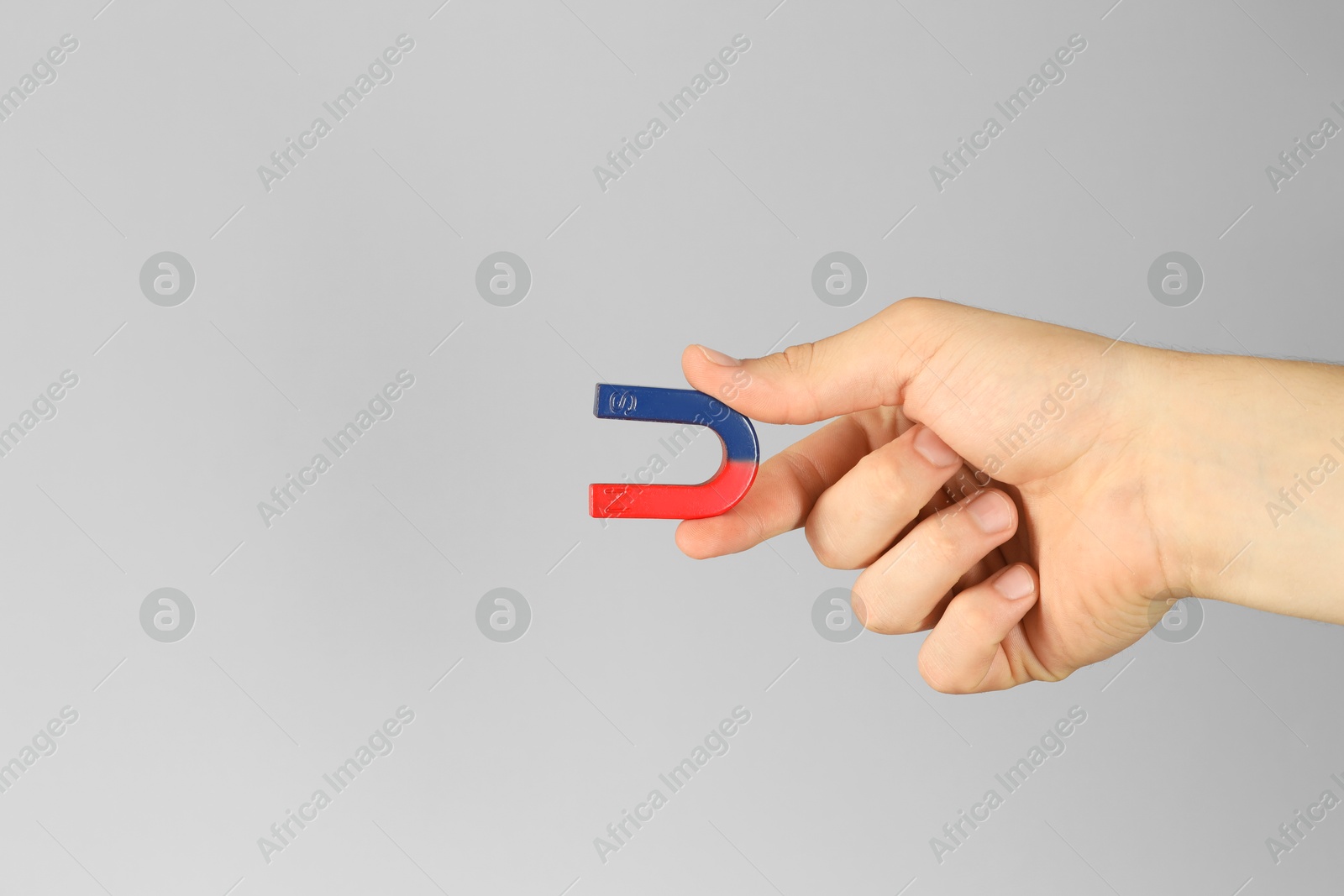 Photo of Man holding horseshoe magnet on grey background, closeup. Space for text