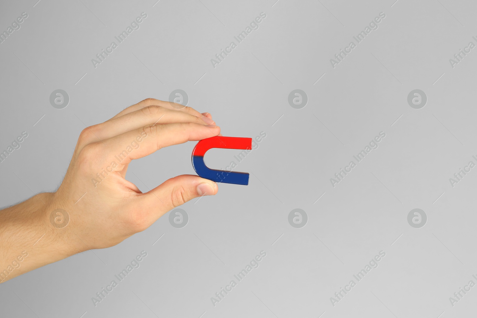 Photo of Man holding horseshoe magnet on grey background, closeup. Space for text