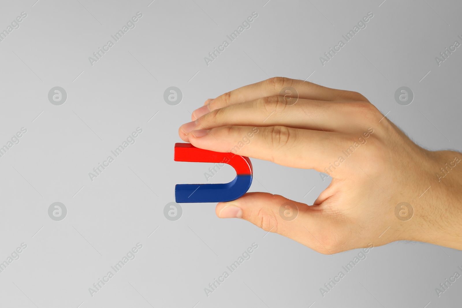 Photo of Man holding horseshoe magnet on grey background, closeup. Space for text