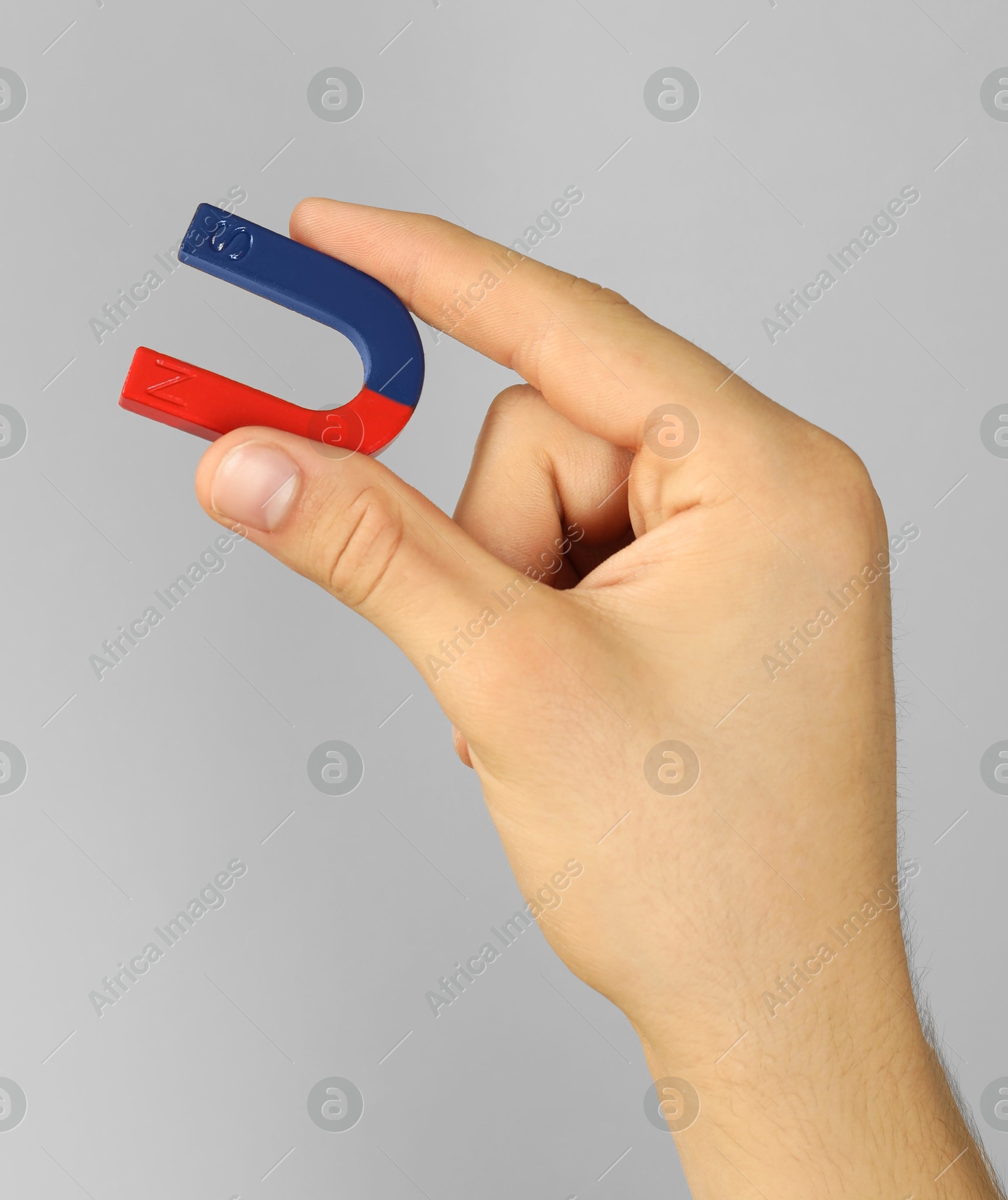 Photo of Man holding horseshoe magnet on grey background, closeup