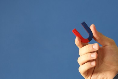 Photo of Man holding horseshoe magnet on blue background, closeup. Space for text