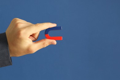 Photo of Man holding horseshoe magnet on blue background, closeup. Space for text