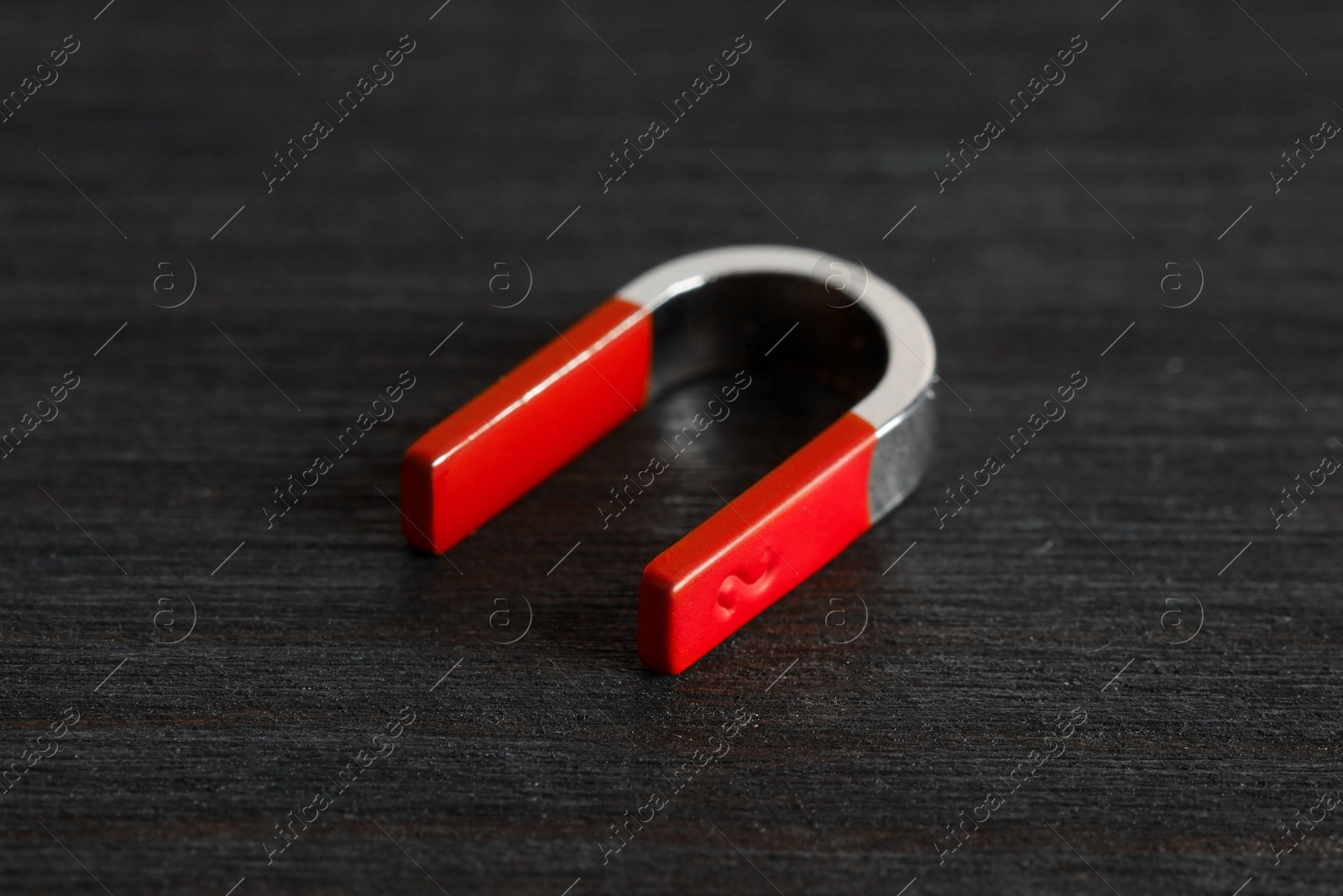 Photo of One horseshoe magnet on black wooden table, closeup