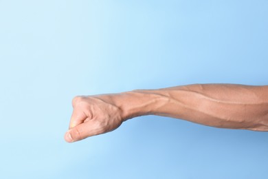 Photo of Man with bulging veins on his arm against light blue background, closeup