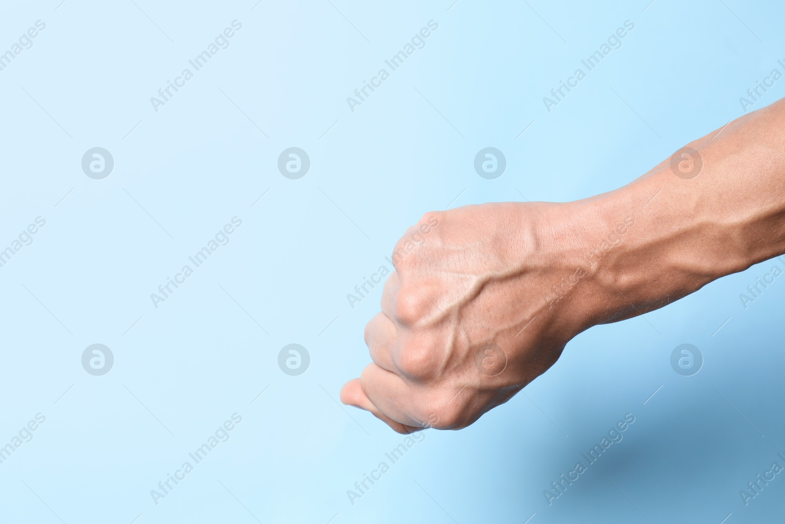 Photo of Man with bulging veins on his arm against light blue background, closeup. Space for text