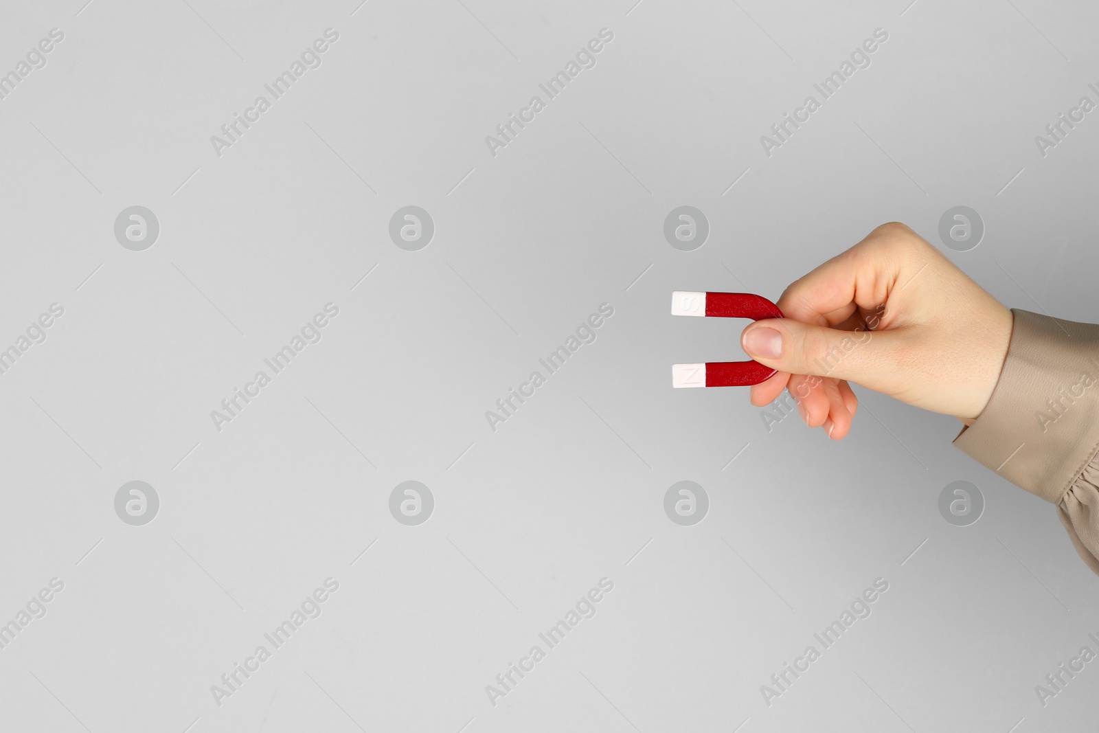 Photo of Woman with horseshoe magnet on grey background, closeup. Space for text