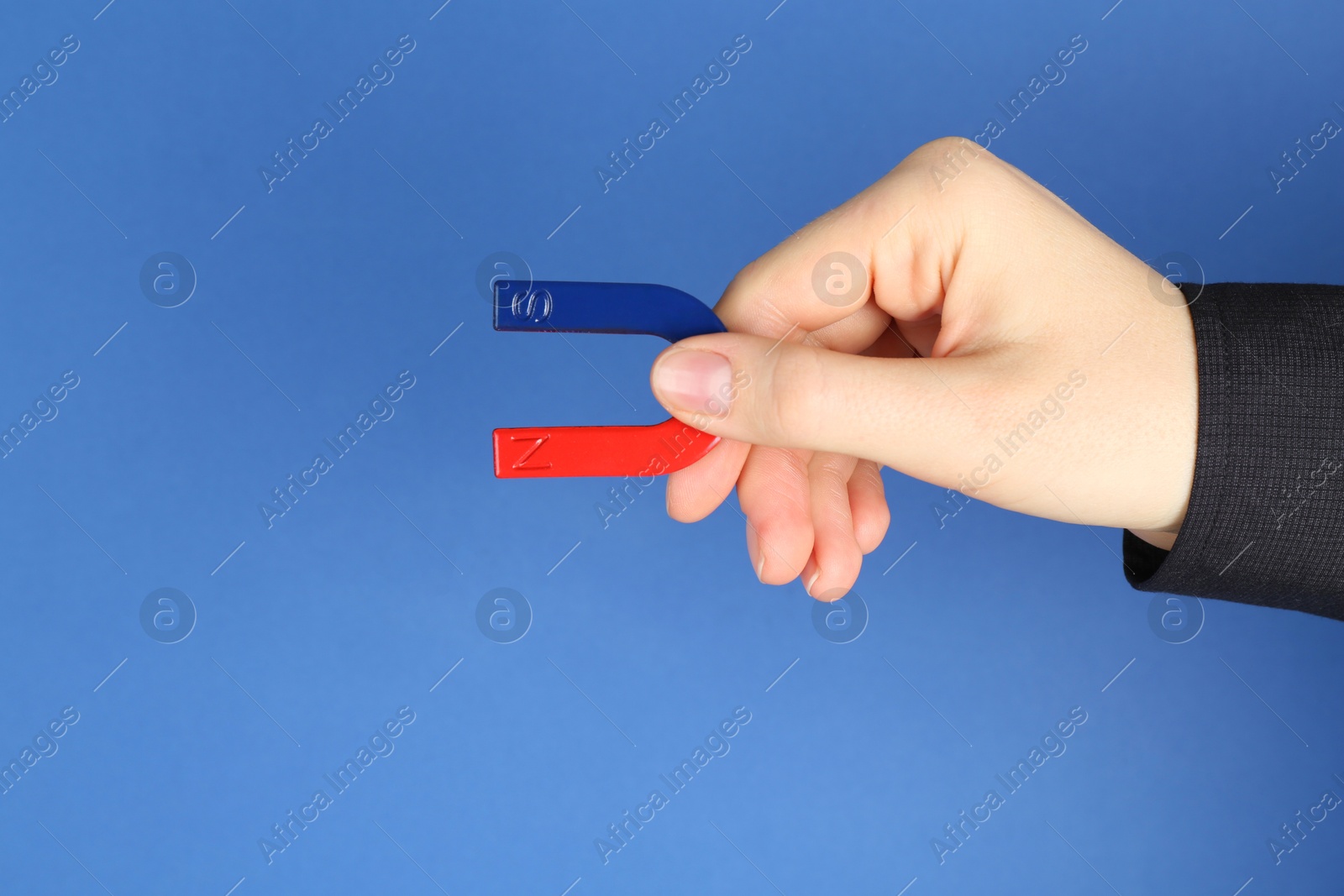 Photo of Woman with horseshoe magnet on blue background, closeup