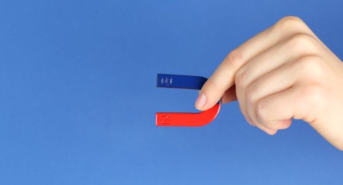 Photo of Woman with horseshoe magnet on blue background, closeup. Space for text