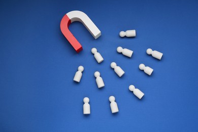 Photo of Magnet attracting human figures on blue background, flat lay