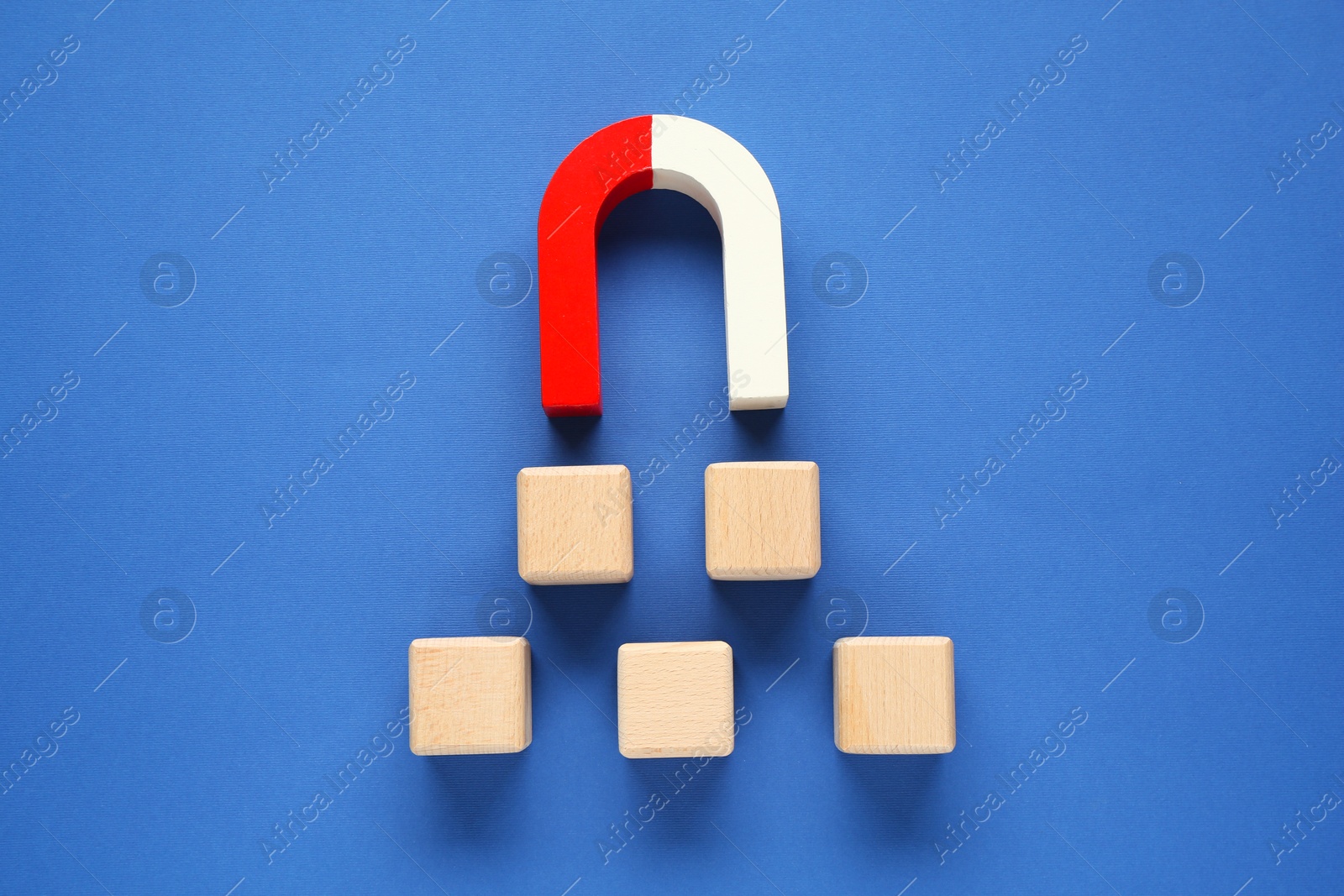 Photo of Magnet attracting wooden cubes on blue background, top view