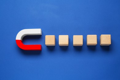 Photo of Magnet attracting wooden cubes on blue background, top view