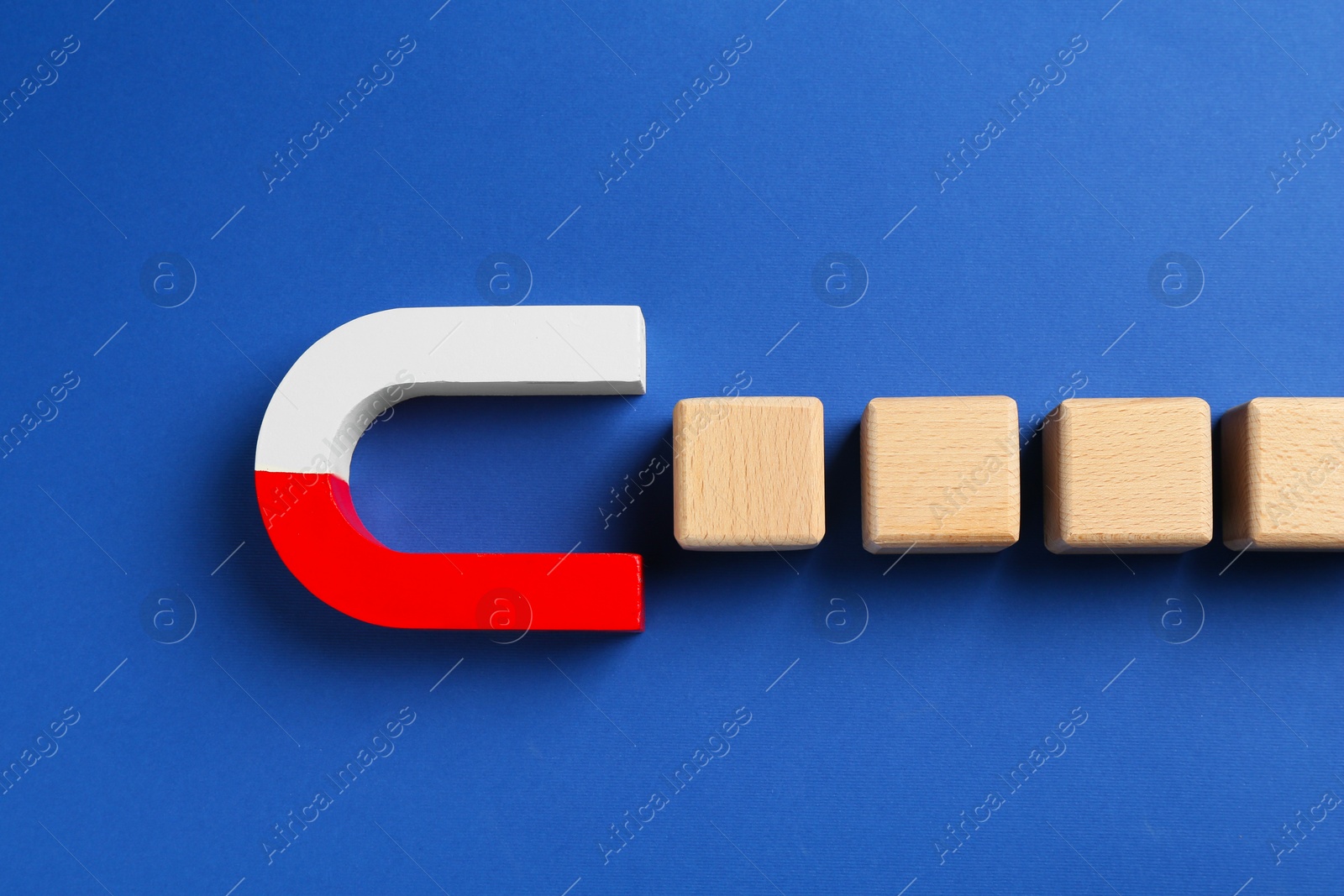 Photo of Magnet attracting wooden cubes on blue background, top view