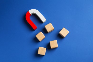 Photo of Magnet attracting wooden cubes on blue background, top view