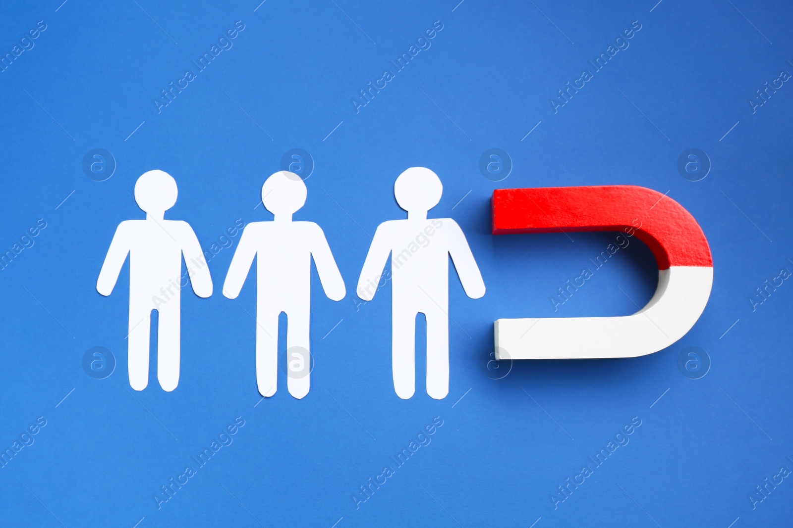 Photo of Magnet attracting paper human figures on blue background, top view