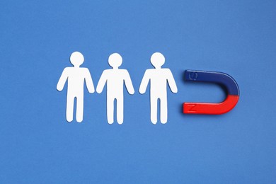 Photo of Magnet attracting paper human figures on blue background, top view